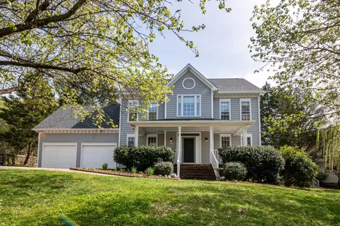 Two-story home framed by mature trees and a green lawn