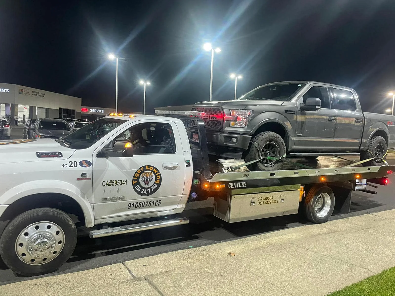 Tiger’s branded white flatbed transporting a pickup under lights at night